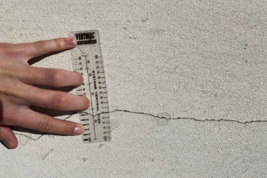 Personne mesurant une fissure avec un mètre ruban.