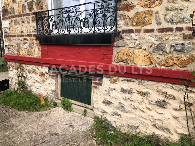 Façades du Lys : mur de pierre avec balcon rouge et fer forgé.