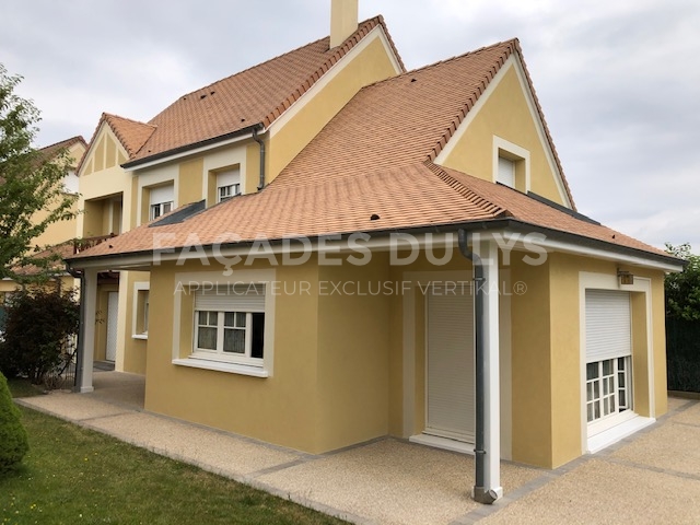 Maison jaune avec toiture brune, fenêtres avec stores.